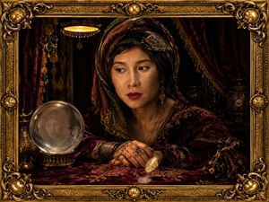 Realistic fortune teller sits in a velvet-draped chamber, framed by ornate gold baroque corners and warm lamplight. Her jeweled hands rest near a spinning coin, while a crystal ball reveals a ghosted portrait. Rich fabrics, tassels, candles, and deep shadows create a mysterious, elegant, cinematic atmosphere for storytelling web art.