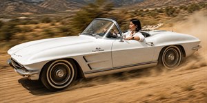 Dust flies as a gleaming white classic convertible tears across a sunbaked country road, driven with effortless confidence and style. The relaxed driver, scarf streaming in the wind, turns every mile into a statement of freedom, speed, and timeless elegance. A bold, cinematic ride that captures adventure in motion beautifully.