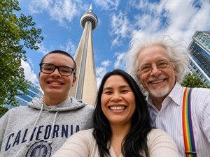 Joyful family selfie beneath Torontos CN Tower, captured with bright sky, city glass, and leafy summer charm. Enhanced smiles, playful Einstein-inspired hair, rainbow suspenders, and crisp detail create a fun, unforgettable portrait. A lively keepsake blending humor, travel, and warmth into a polished promotional hand-painted memory for lasting family joy.