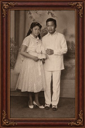 Beautifully restored vintage studio portrait captures a poised couple in elegant formal attire, preserved with warm sepia tones and refined detail. A rich rosewood frame with gold inlay and ornate corners adds heirloom charm, creating a timeless keepsake ready to display, celebrate family history, and treasure for generations to come.