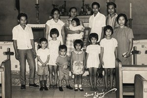 A beautifully restored vintage family portrait captures generations gathered in a warm church setting, rich with history, dignity, and quiet emotion. Enhanced detail reveals expressive faces, timeless clothing, altar candles, wooden pews, and treasured heritage, creating a meaningful keepsake that celebrates family, memory, and enduring love.